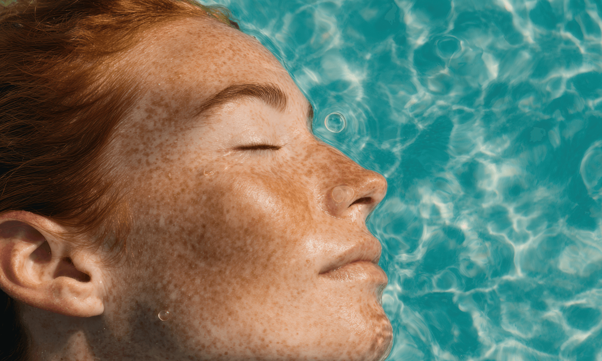 Macchie solari: prevenzione e trattamenti Primo piano del viso di una donna lentigginosa che galleggia in acqua con gli occhi chiusi, immagine evocativa dei segni lasciati dal sole sulla pelle e dell’importanza di trattare le discromie cutanee.