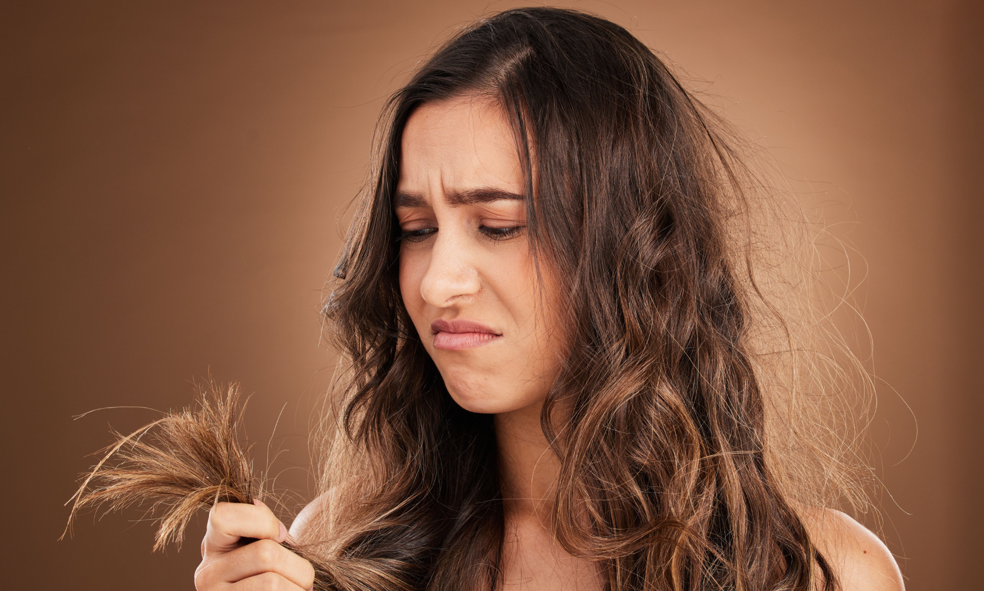 Primavera e capelli più deboli: riconosci i segnali e intervieni per tempo Donna che osserva con espressione preoccupata le punte dei capelli secchi e sfibrati, immagine che rappresenta capelli indeboliti e fragili nel cambio di stagione.
